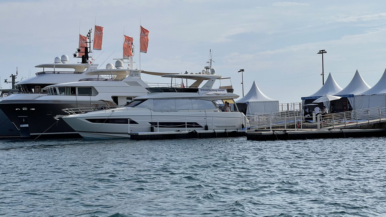 Motor yachts moored at a boat show pontoon with white exhibitor tents