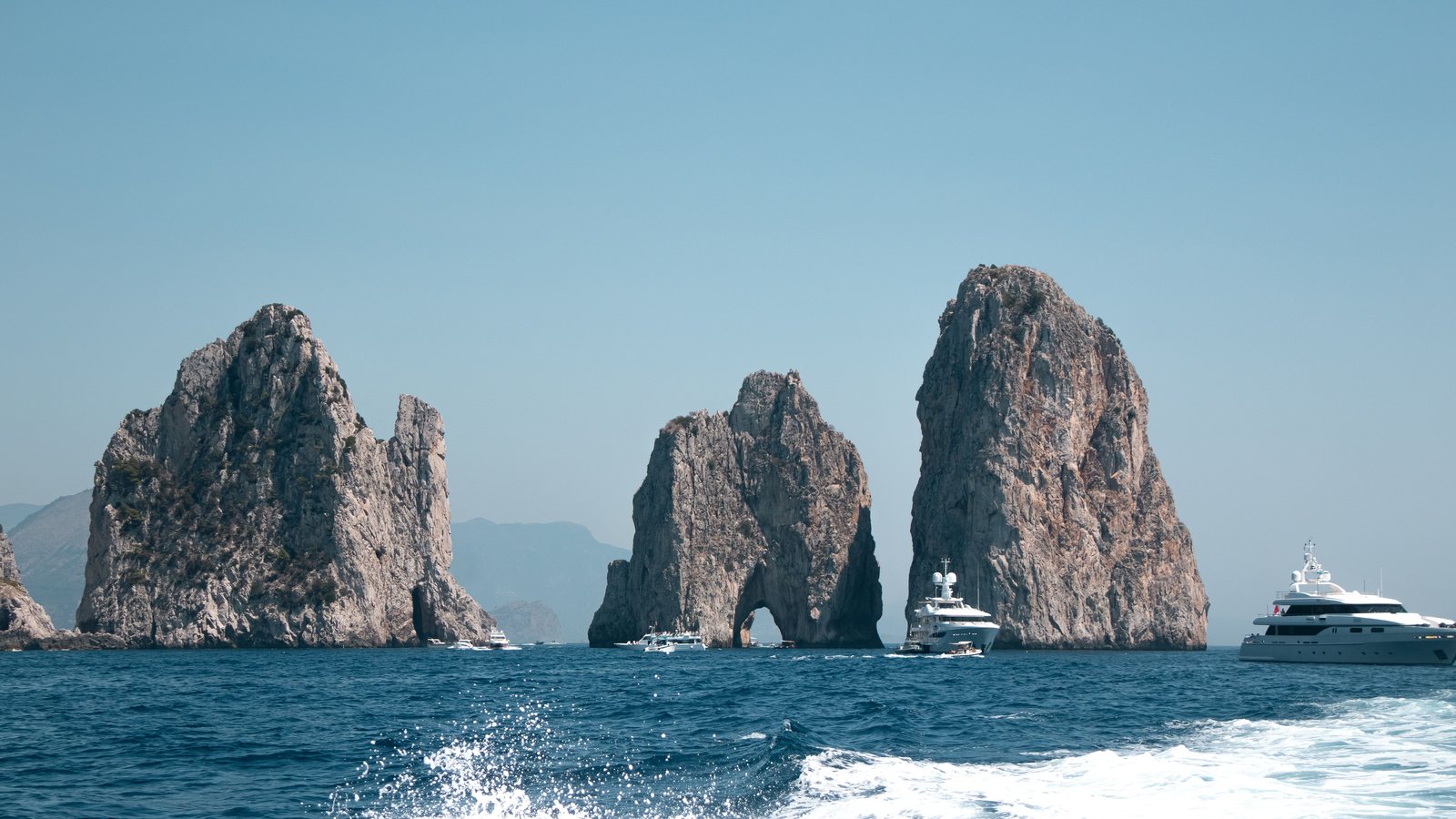 Superyachts at anchor beside the Faraglioni rocks off Capri, seen from a moving boat