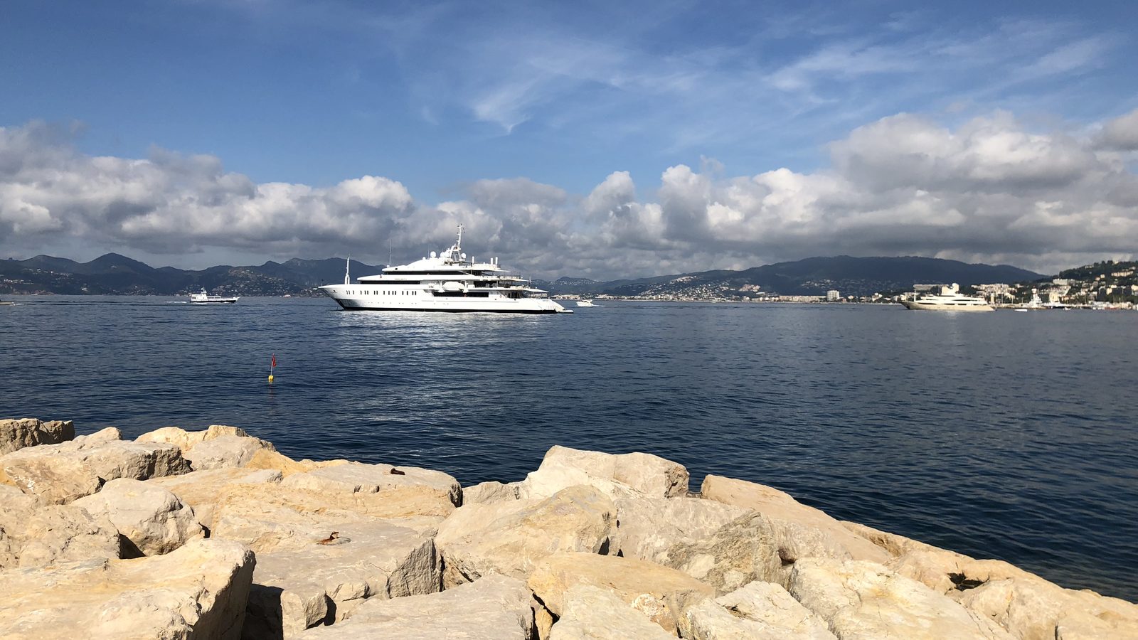 A large superyacht at anchor in the bay, rocks in the foreground