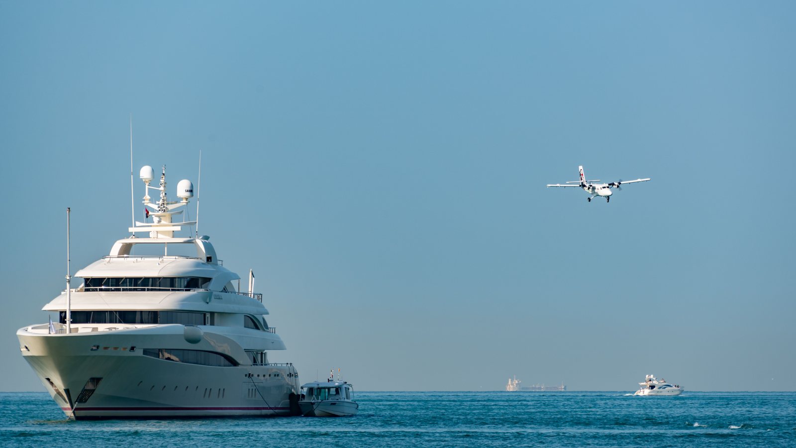 Superyacht at anchor with communication domes on its mast, a seaplane flying past