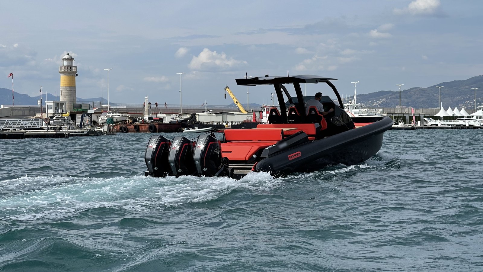 A large black and orange tender with three outboard engines leaving a harbour past a lighthouse