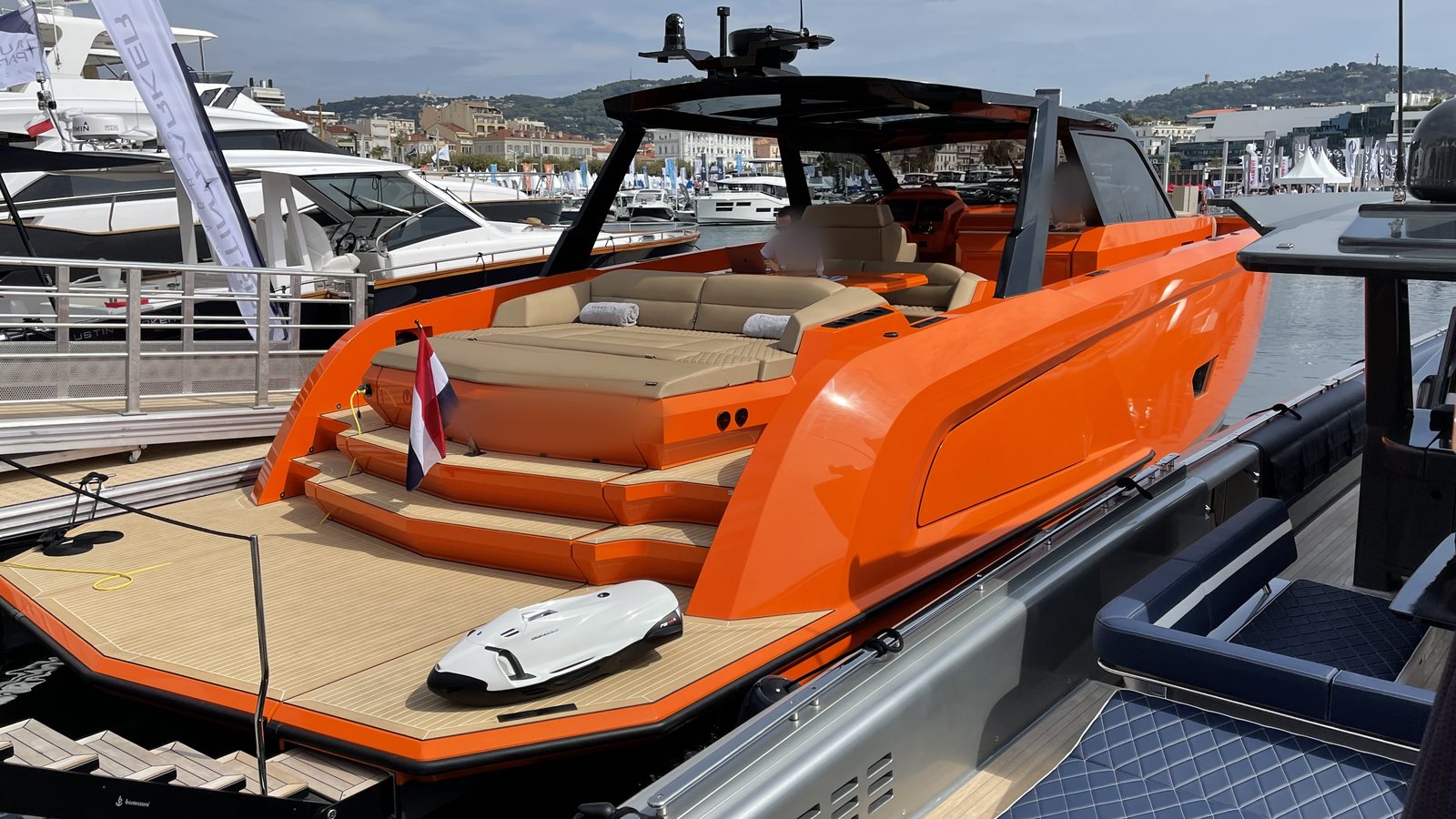 Orange chase boat with teak swim platform and an underwater scooter on deck, moored at a boat show